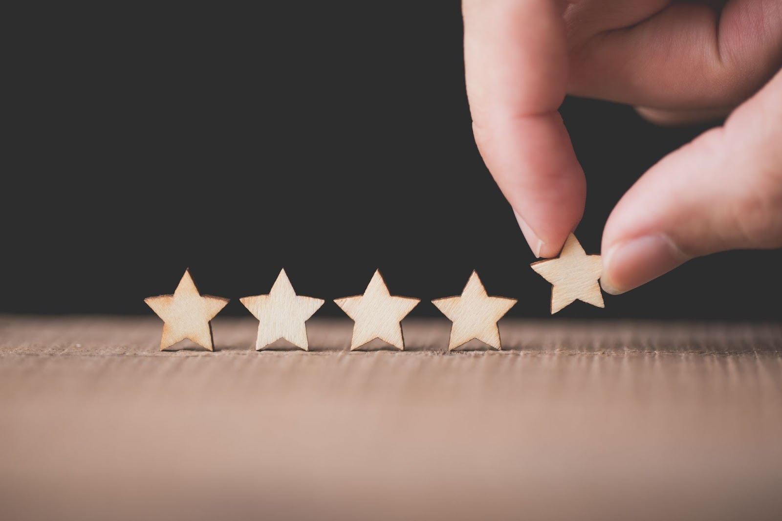 A hand carefully placing down a row of small wooden stars, which look similar to an online review score
