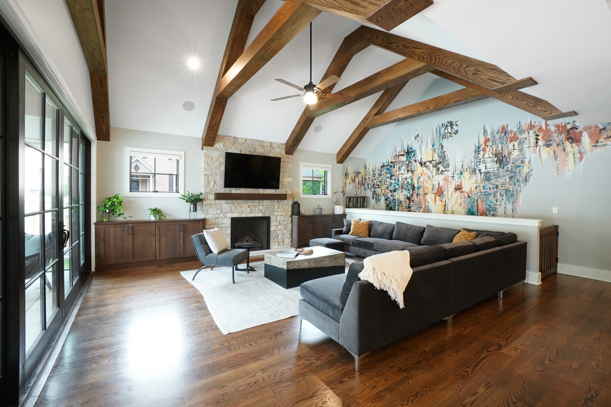 Living room with wood beam vaulted ceilings, stone fireplace and built-in cabinetry. Featuring a painted mural.