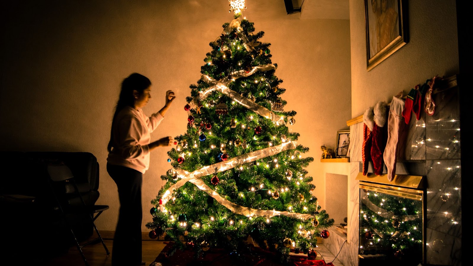 Woman decorates lit christmas tree at night in home