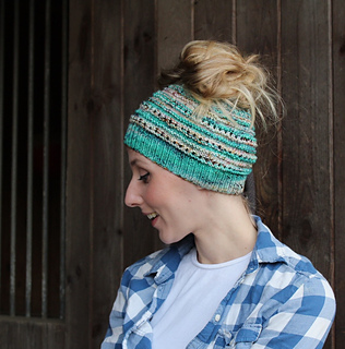 woman wearing striped messy bun beanie knitting pattern in front of dark wooden background