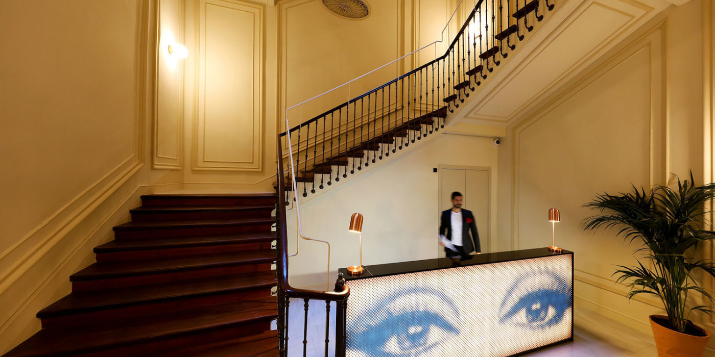 The lobby of Axel Hotel Madrid with beige walls and a carpeted staircase via Axel Hotel Madrid