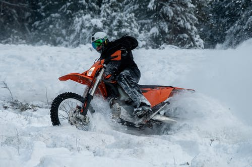 A man riding a red dirt bike in winter snow. It is not advisable to ride motorbikes in the snow because of slipperiness.