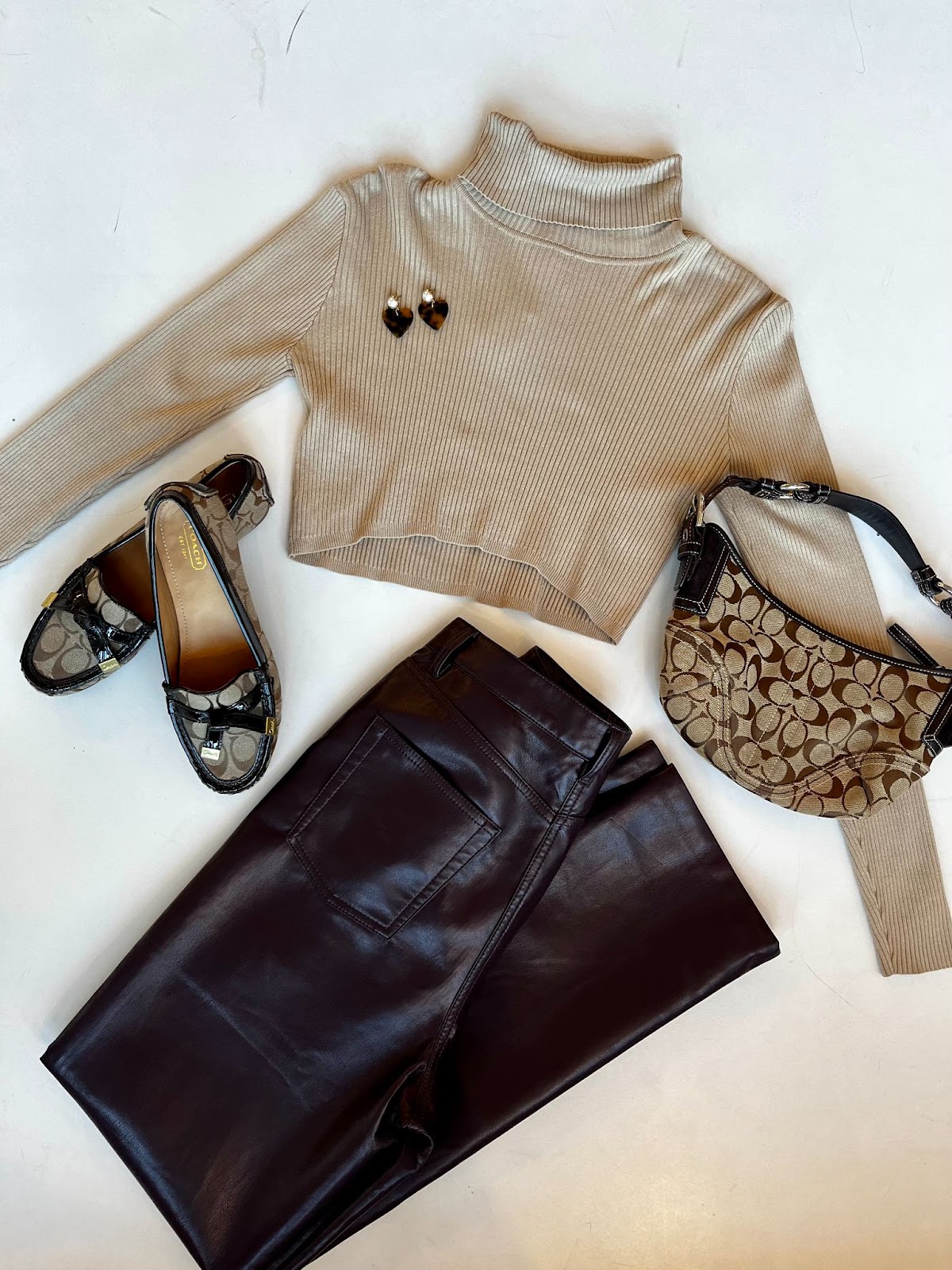 an image of some capsule wardrobe pieces from peacock boutique. the clothes include a beige turtleneck, black pants and coach accessories 