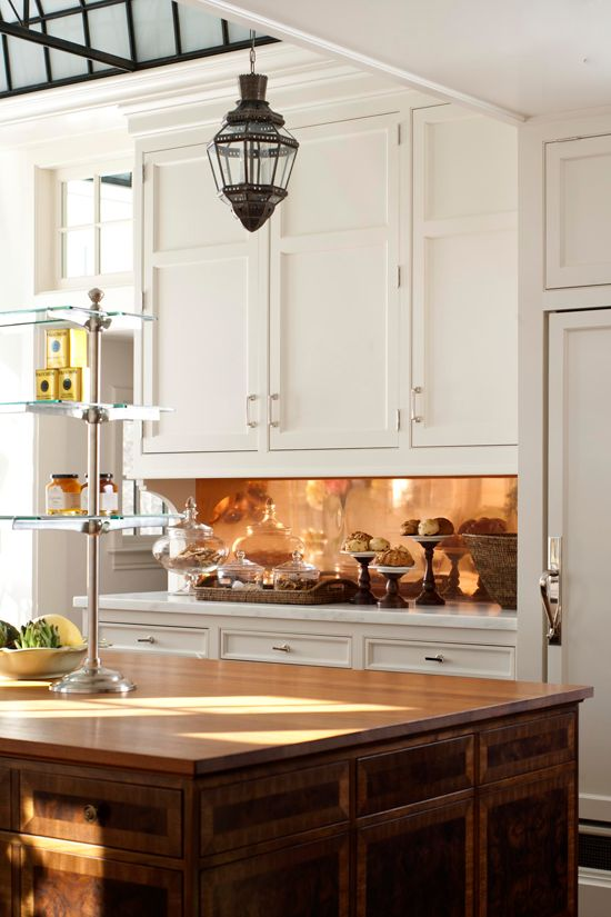 large kitchen with copper backsplash, dark wood center island and white shaker kitchen cabinets