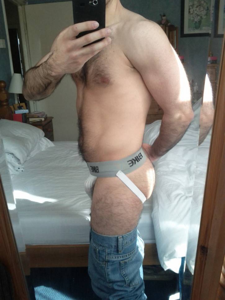 hairy gay male otter taking an android mirror selfie in a white jockstrap shirtless with his blue jeans pulled down to his knees