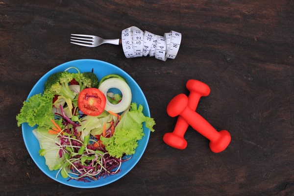 Salad served on a blue plate with dumbbells and a fork on the side, placed on a wooden surface