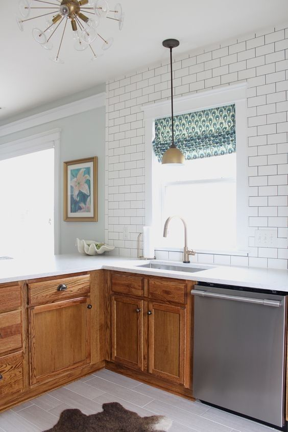 By keeping the kitchen cabinets in their original oak finish, this kitchen gets a bright white makeover with sleek grey floor tiles and modern-day appliances.  90s Oak kitchen cabinets with grey tile floor and white subway tile.