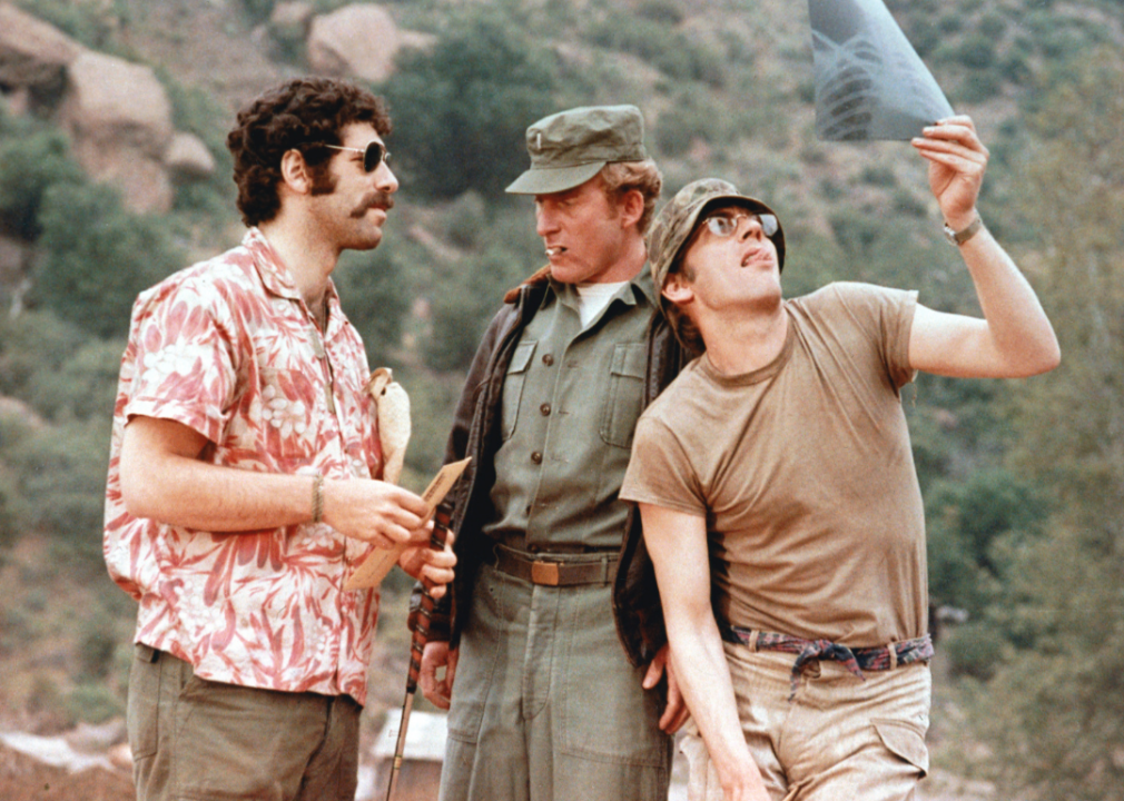 Elliot Gould talking with a uniformed officer and Donald Sutherland examining an x-ray in a publicity still from ‘MASH’.