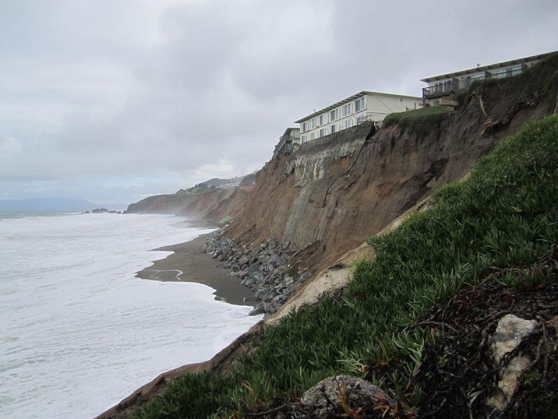 House on top of a crumbling cliff above ocean waves