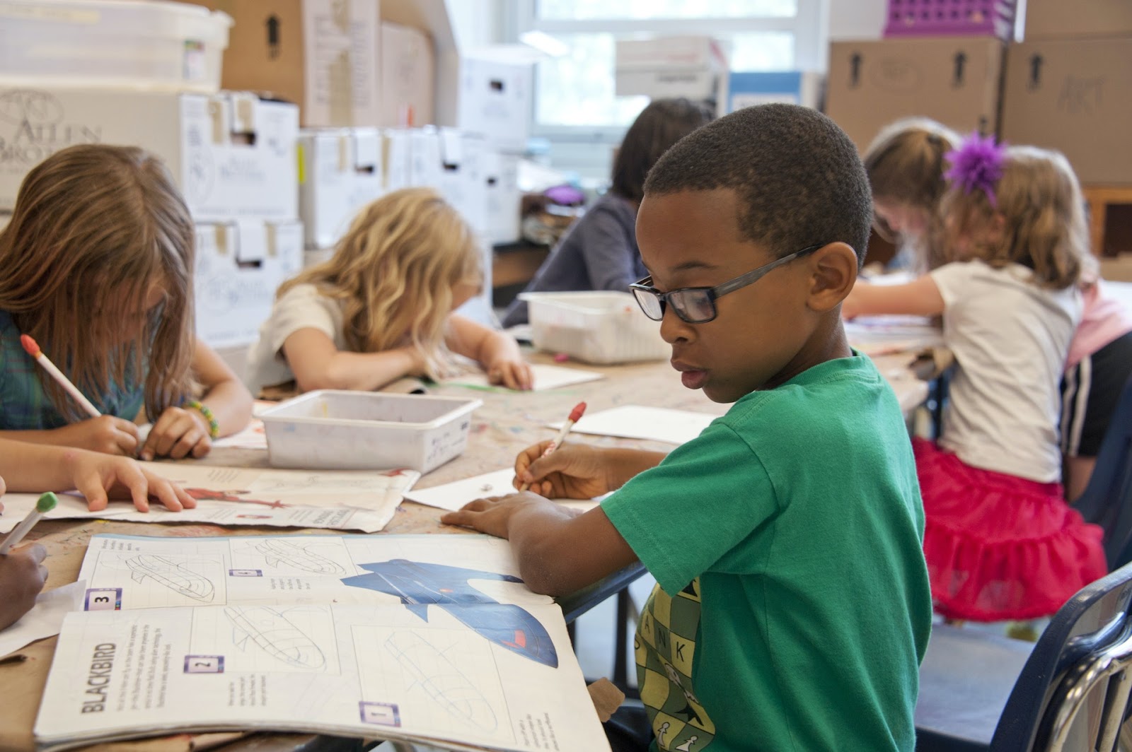 Kids participate in group activities, studying animals. There is a boy in a green shirt studying a book about blackbirds. This could be biology focused STEM club for kids.