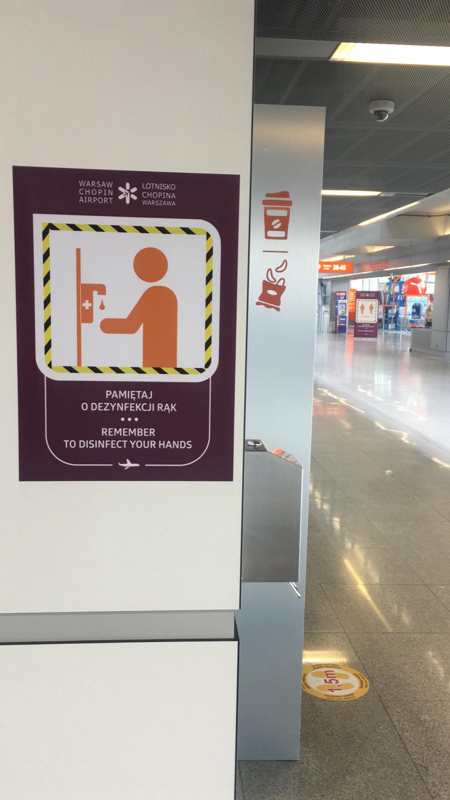 Warsaw Chopin Airport COVID-19 purple poster reminding passengers to disinfect their hands. How coronavirus pandemic changed airplane travel.