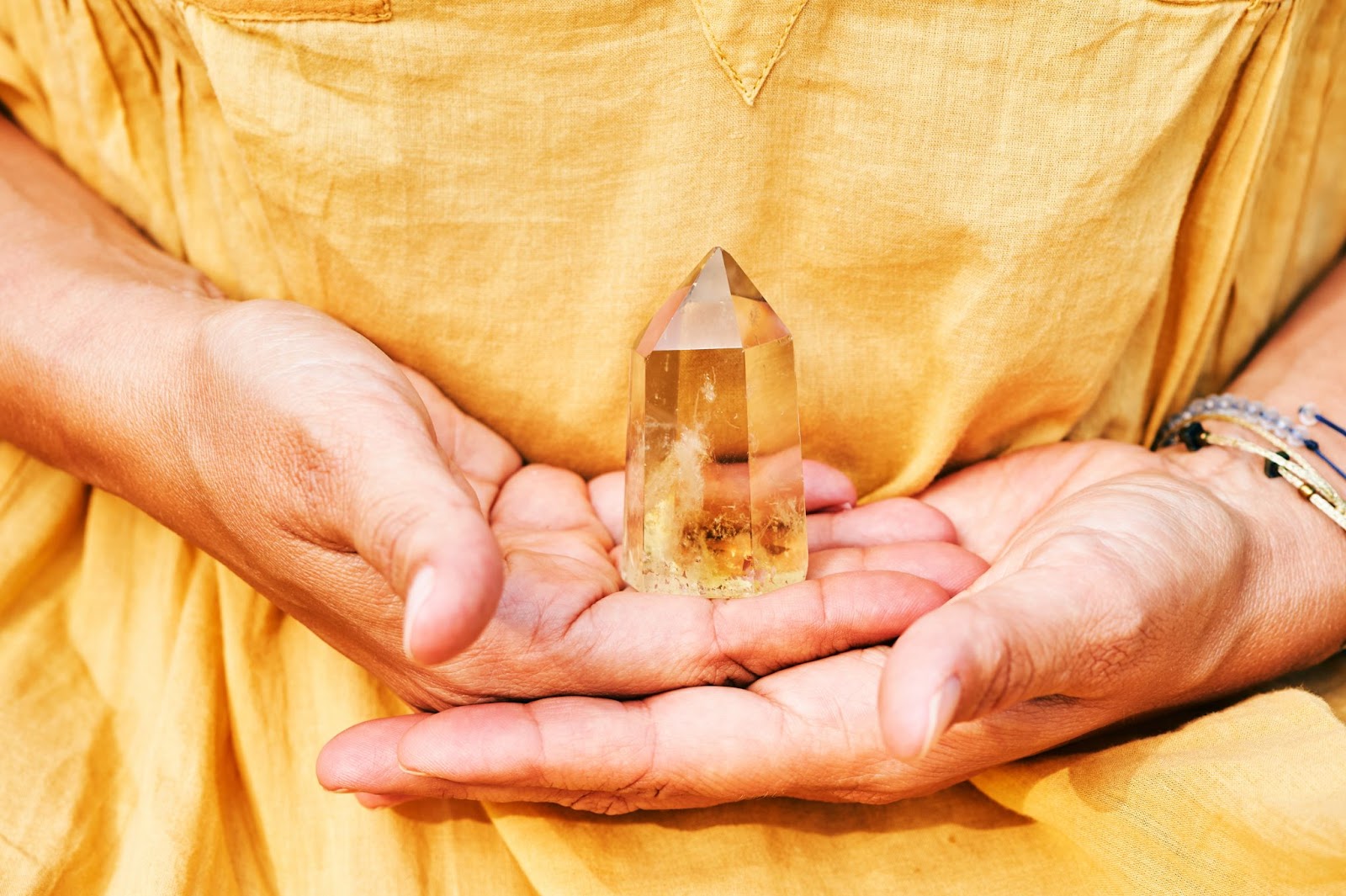 A bright yellow citrine crystal held in the hands of someone wearing a yellow t-shirt. 