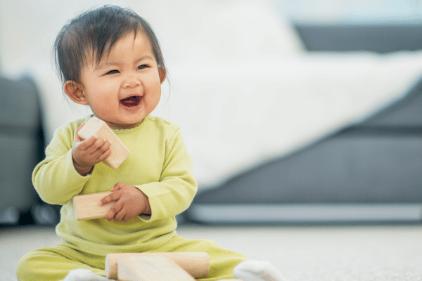 Smiling baby sitting upright and playing with wooden blocks.