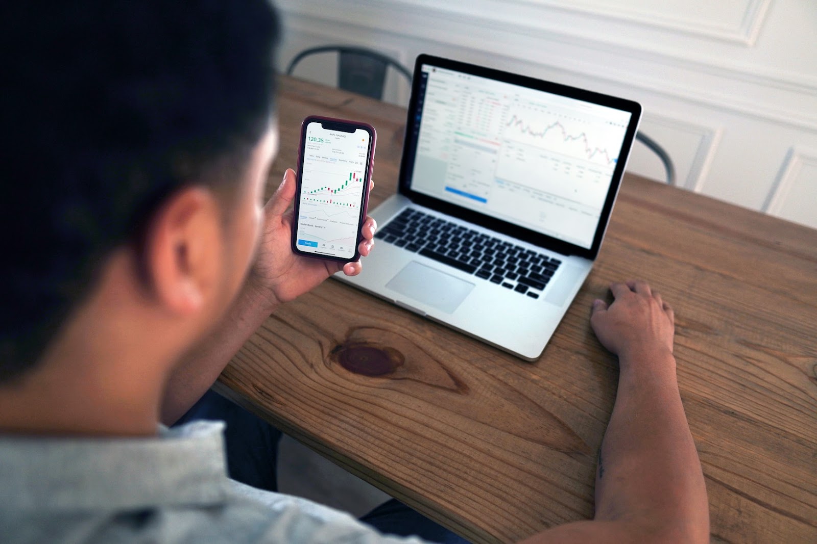 a person looking at trading charts from a phone and laptop 