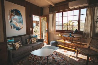 A living room with a large window and a gray sofa sitting next to an open door