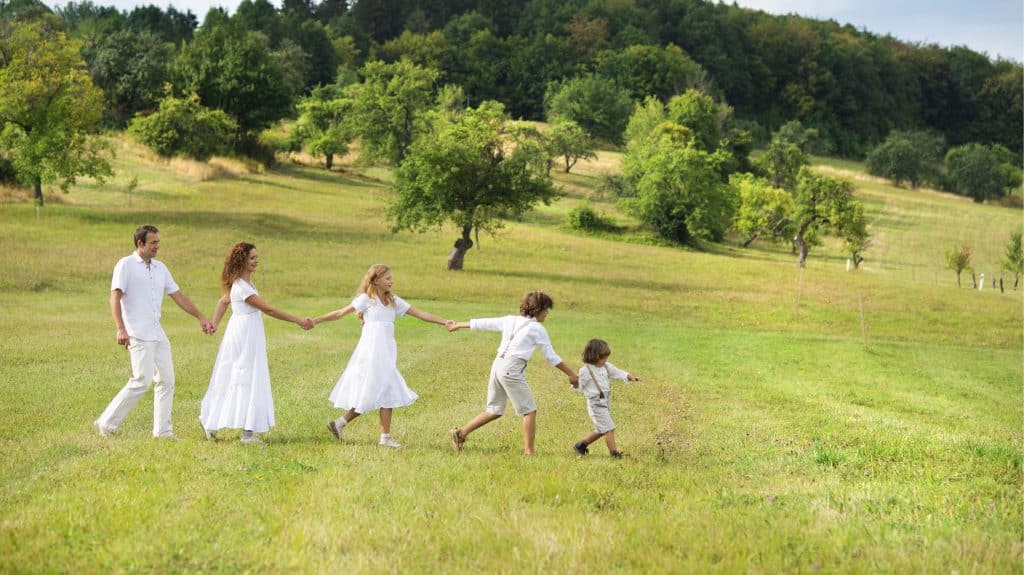 famille-nombreuse-tableau-d-organisation-famille-nombreuse : deux parents et trois enfants habillés en blanc se tiennent par la main en marchant dans la nature