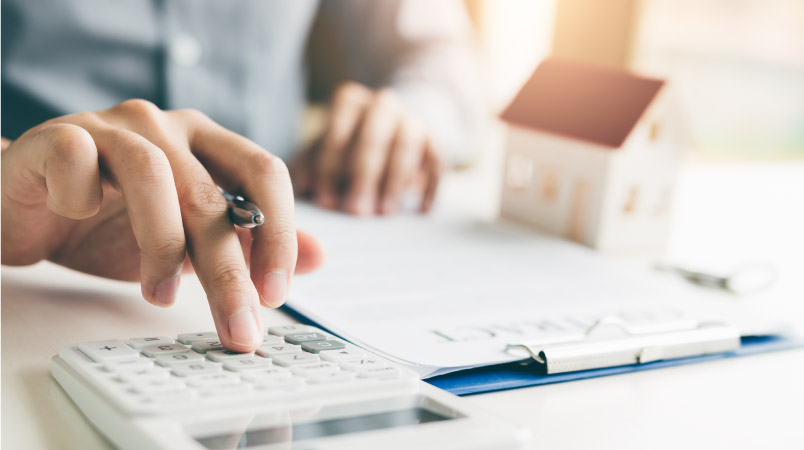 A man using a calculator to determine his monthly expenses based on a higher mortgage rate from inflation.