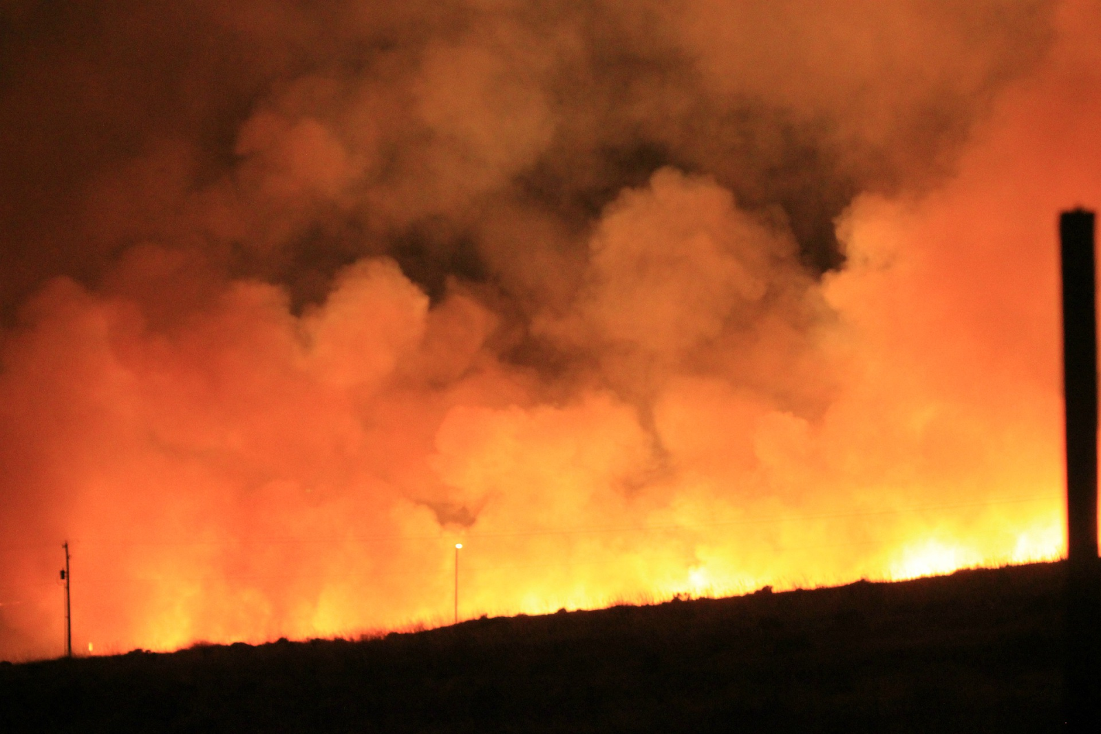 Dark horizon line with wildfire beyond and huge billows of orange smoke