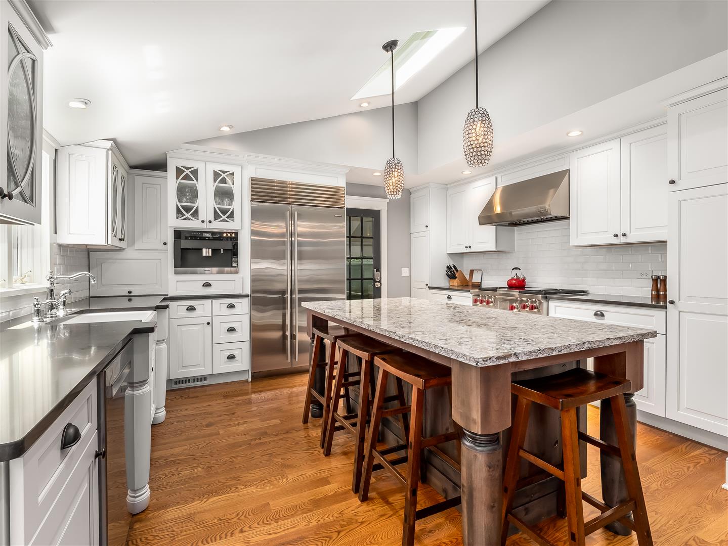 White Kitchen with Decorative Glass Upper Cabinet Doors stainless steal appliances,, contrasting dark quartz countertops and a natural wood stain island/eat-in bar.