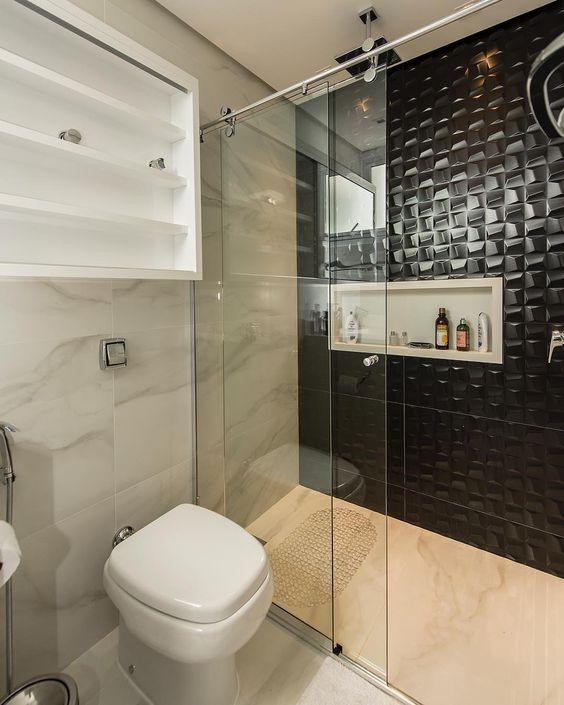 Banheiro com piso e azulejos de porcelanato marmorizado em tom claro e uma parede do box com revestimento preto em 3D.