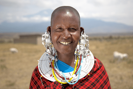 A massai woman smiles to camera wearing elaborate ear rings.