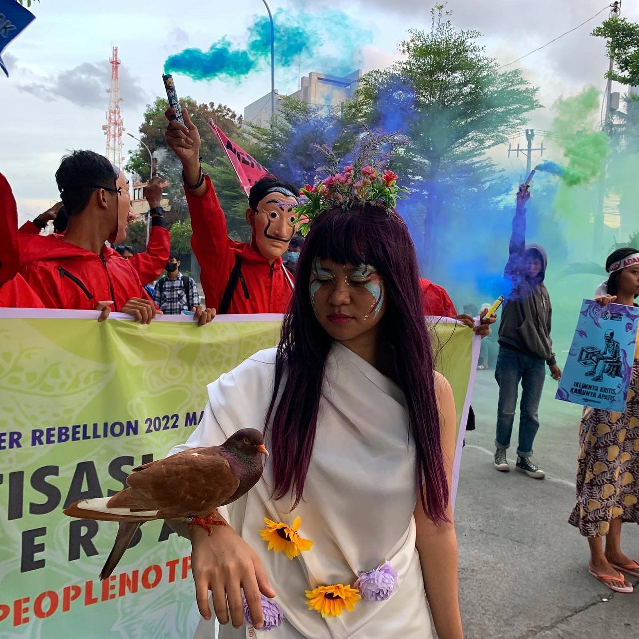 A woman in white robes and a pigeon on her arm leads a colourful rally down an Indonesian main road