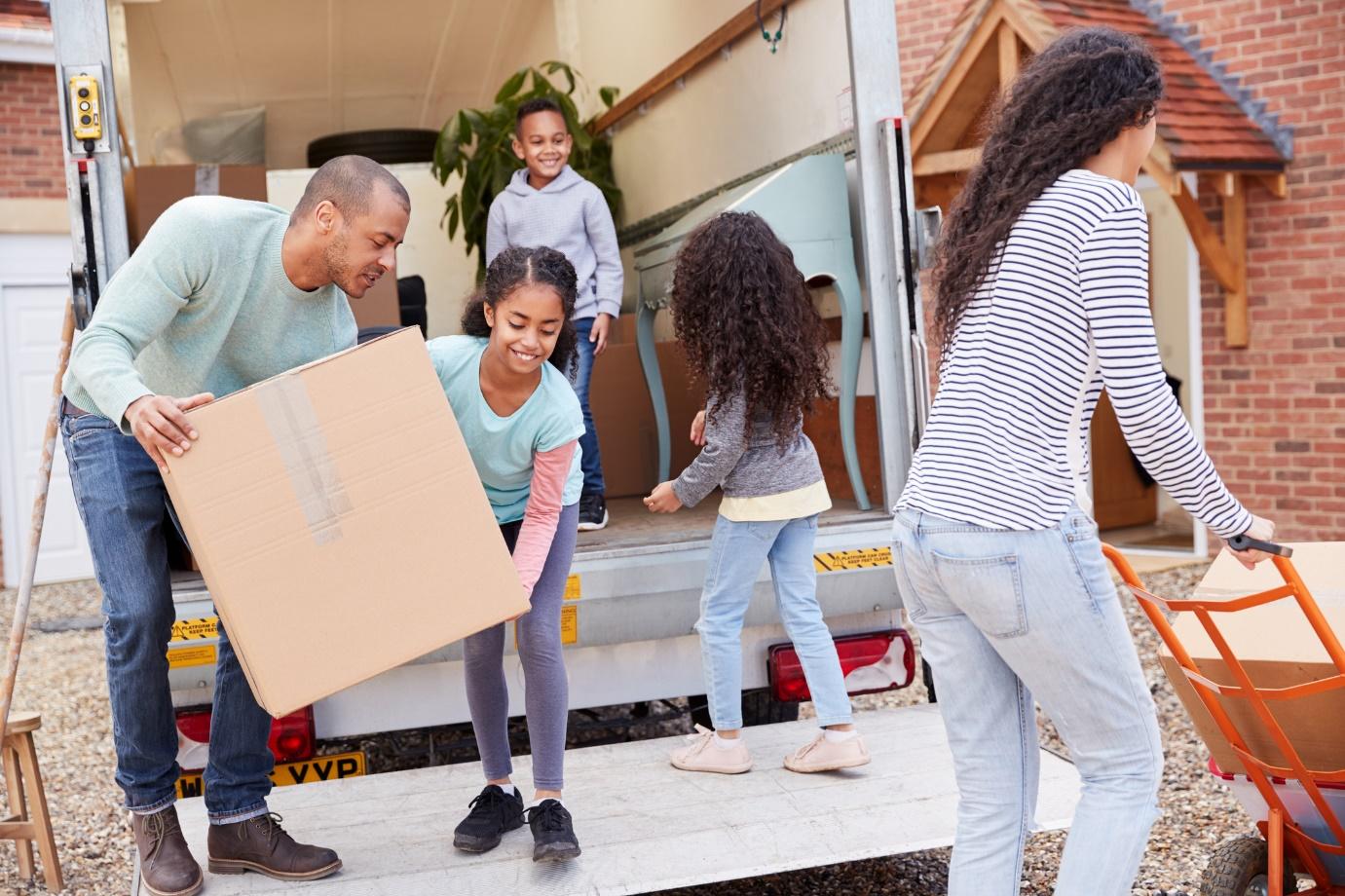 family unloading boxes from a moving company van outside a new house