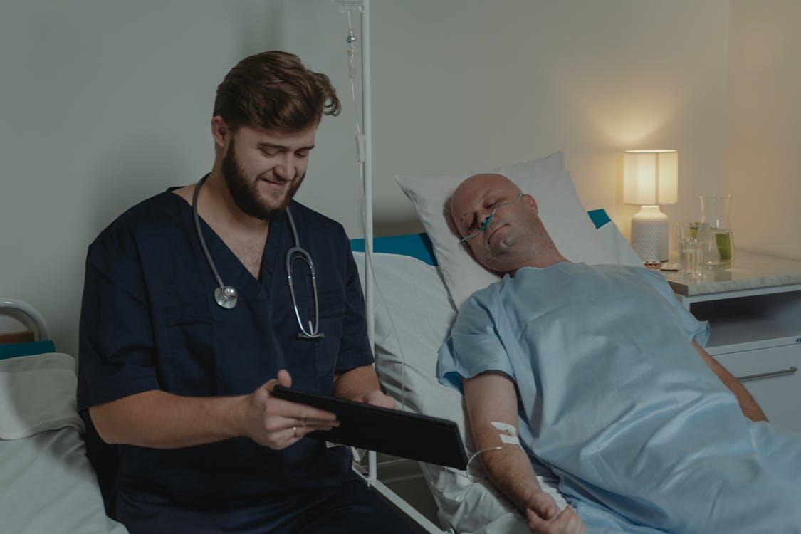 Man in Blue Scrub Suit Sitting on Hospital Bed