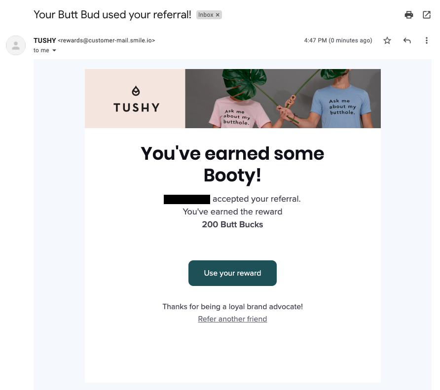 Creative Reward Points Names–A screenshot of one of Tushy’s referral program emails. The email banner shows their logo, with two people wearing pink and blue shirts that say, “Ask me about my butthole”. The email copy reads, “You’ve earned some Booty! NAME accepted your referral. You’ve earned the reward 200 Butt Bucks. Use your reward. Thanks for being a loyal brand advocate! Refer another friend”. 