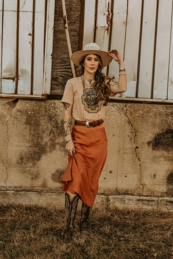 a lady donning a midi skirt, tee, belt, and a cowgirl hat