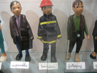 3 dolls in career-related outfits, labeled (in French) computer scientist, firefighter, and photographer