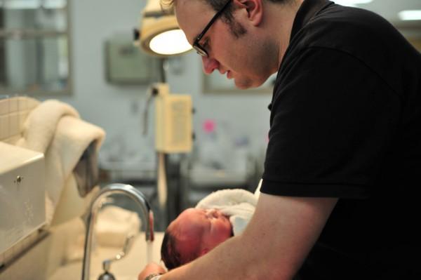 A man washing his baby's hair under a fawcet.