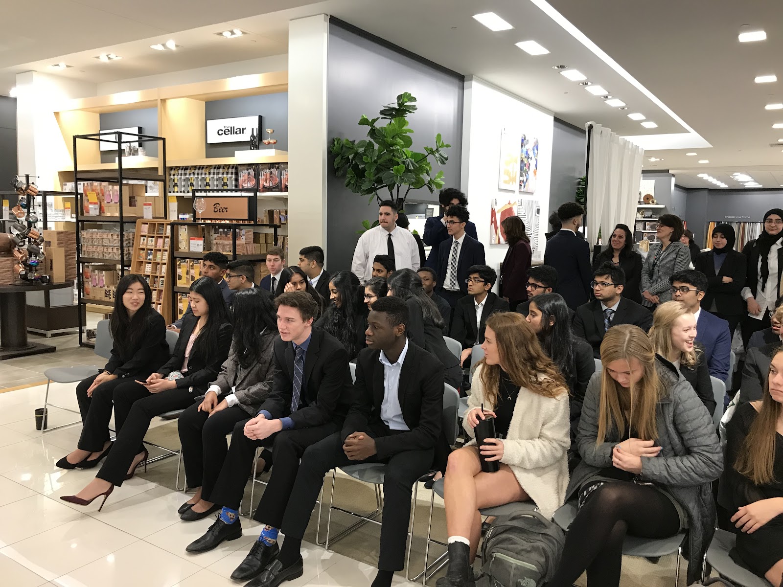 Students from Novi High school seated and Fordson students standing behine them waiting for a presentation.