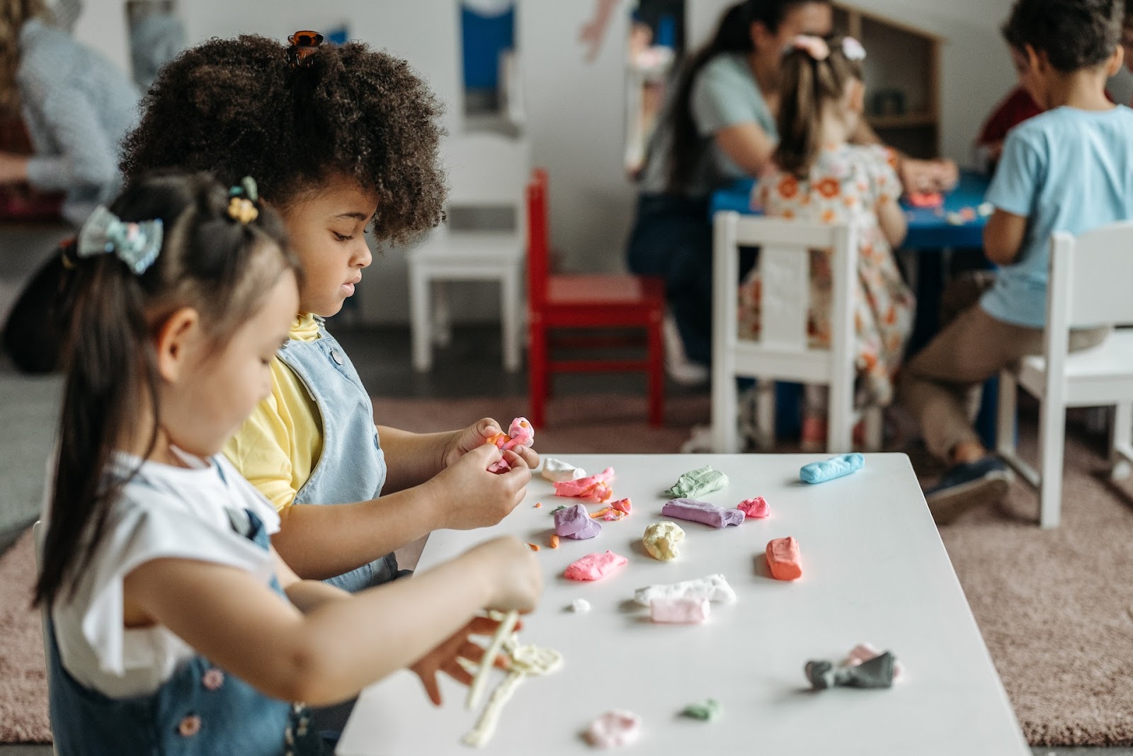 Two young toddler girls playing with clay at a small table