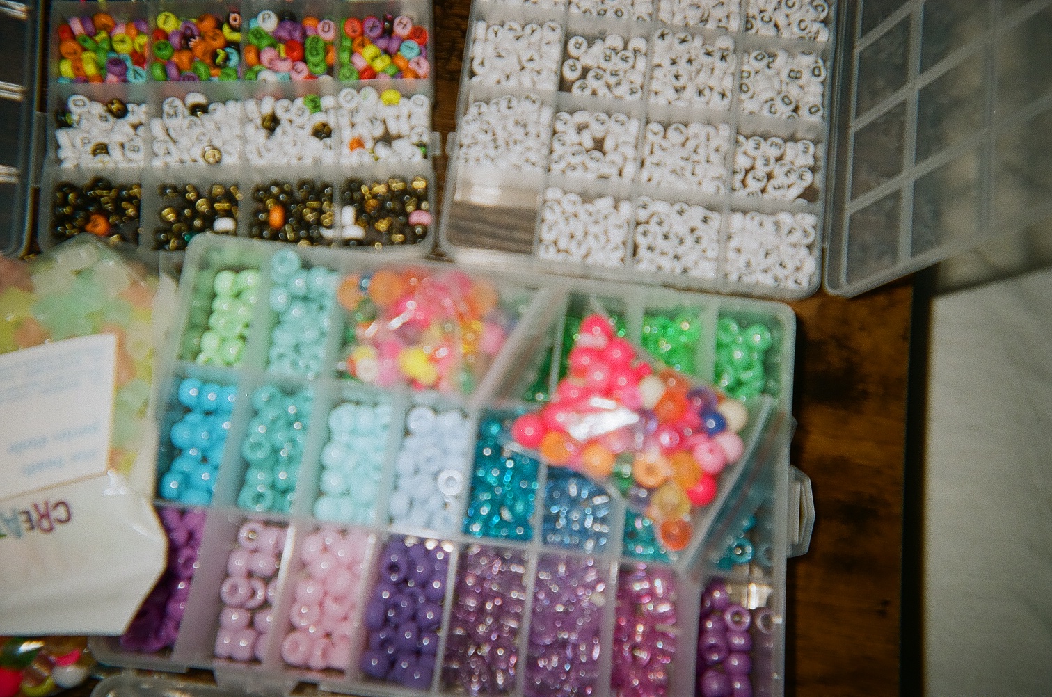 Three boxes of colorful beads and letter beads on top of a table.