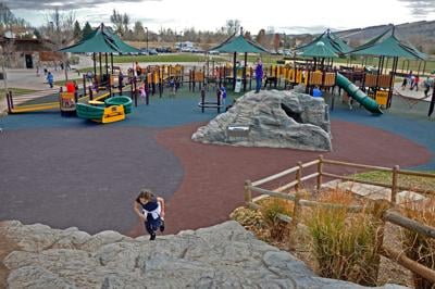 A child runs up a rock structure beyond the large playground equipment at Spring Canyon Park