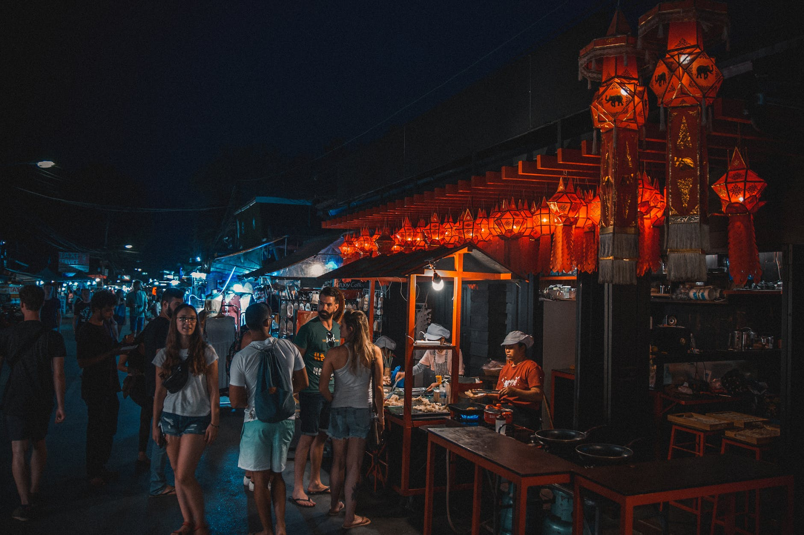 Tourists shopping at a night market in Koh Samui. There are various stalls selling food and souvenirs.