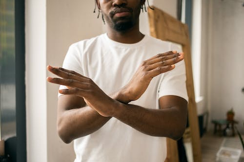 Free Crop unrecognizable bearded African American male in white t shirt demonstrating no gesture with hands while standing in light room Stock Photo