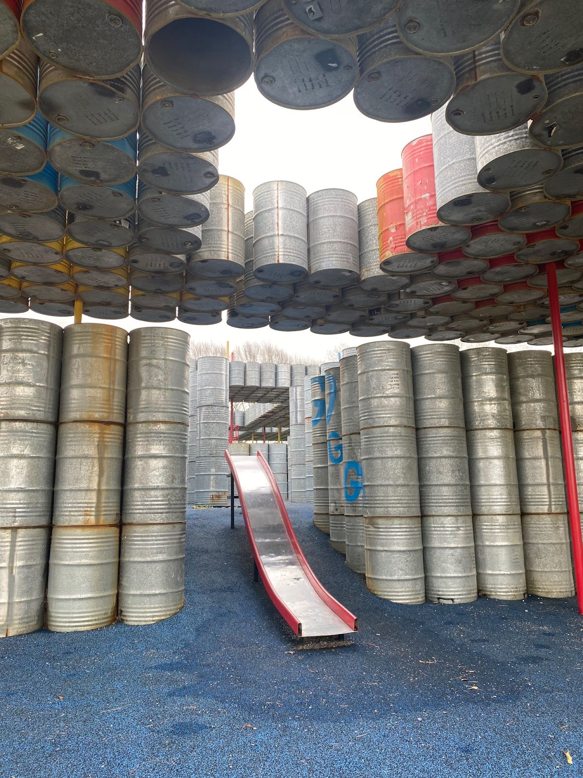 An image of the playground where a slide runs through a gap in the oil drums. 
