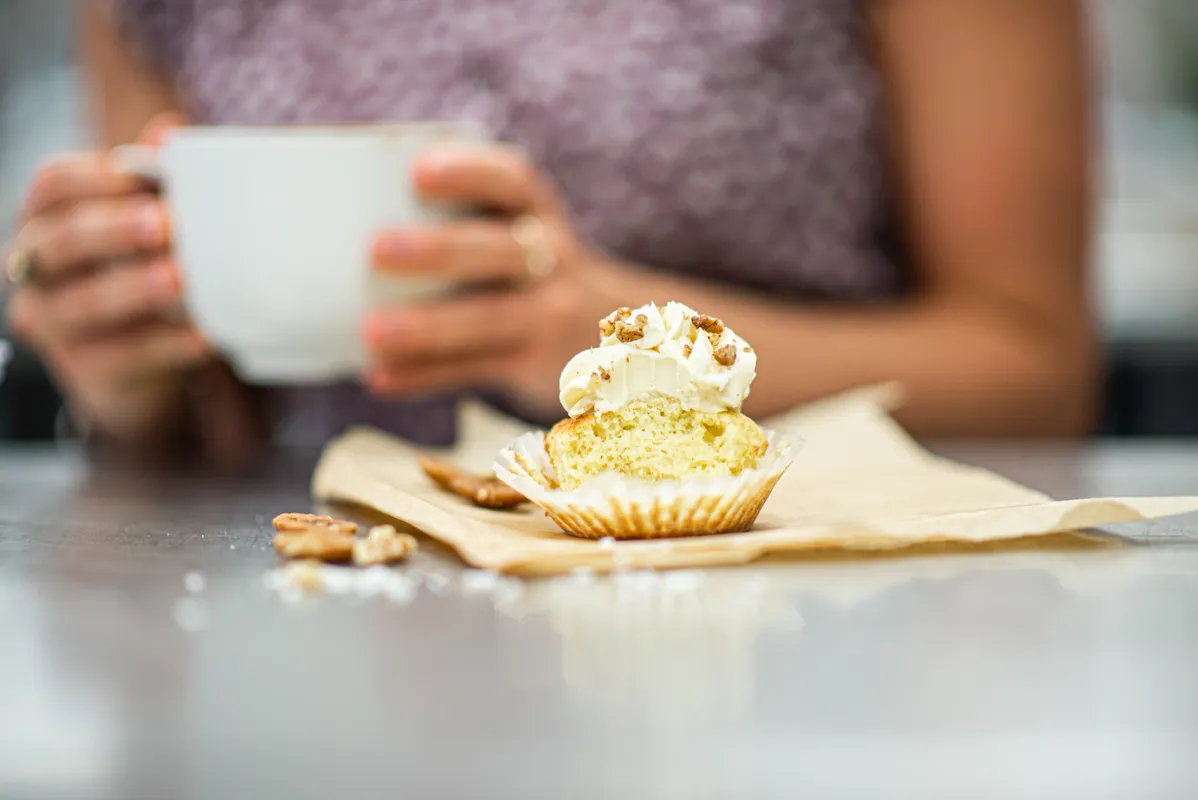 a half-eaten cupcake sits on a table in front of a person drinking coffee