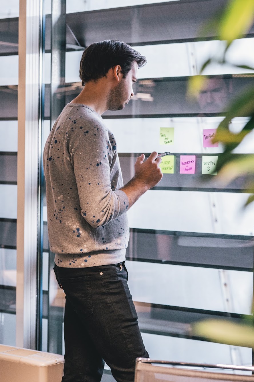 A man standing and writing his tasks on colorful post-it notes