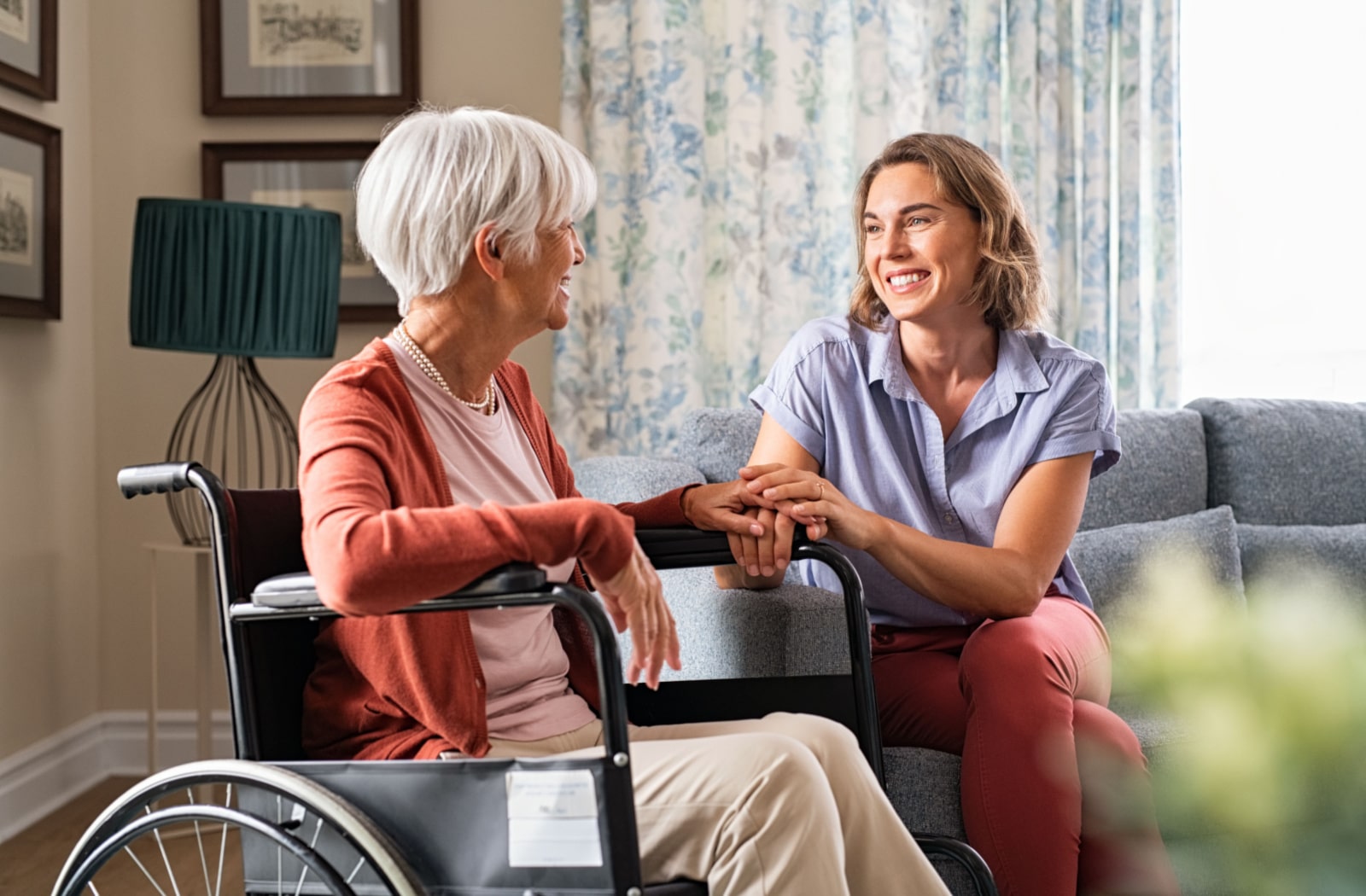 A younger female relative speaking with an older senior living resident and holding her hand