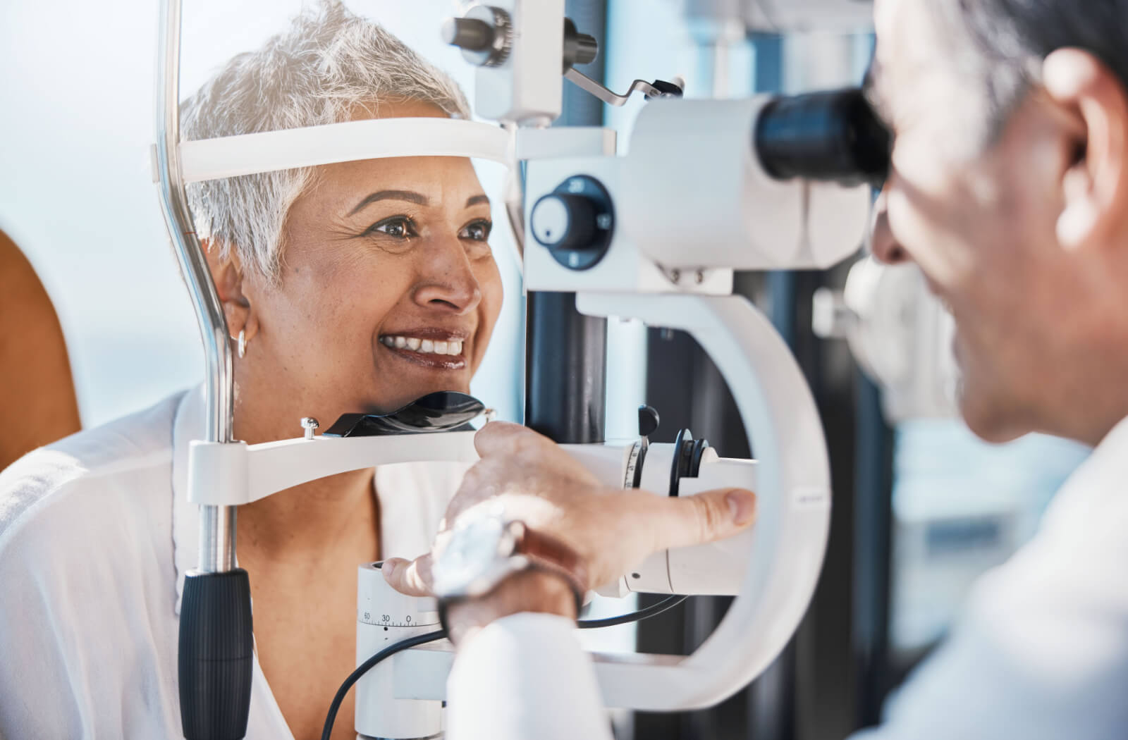 A male optometrist examines a smiling senior woman's eyes
