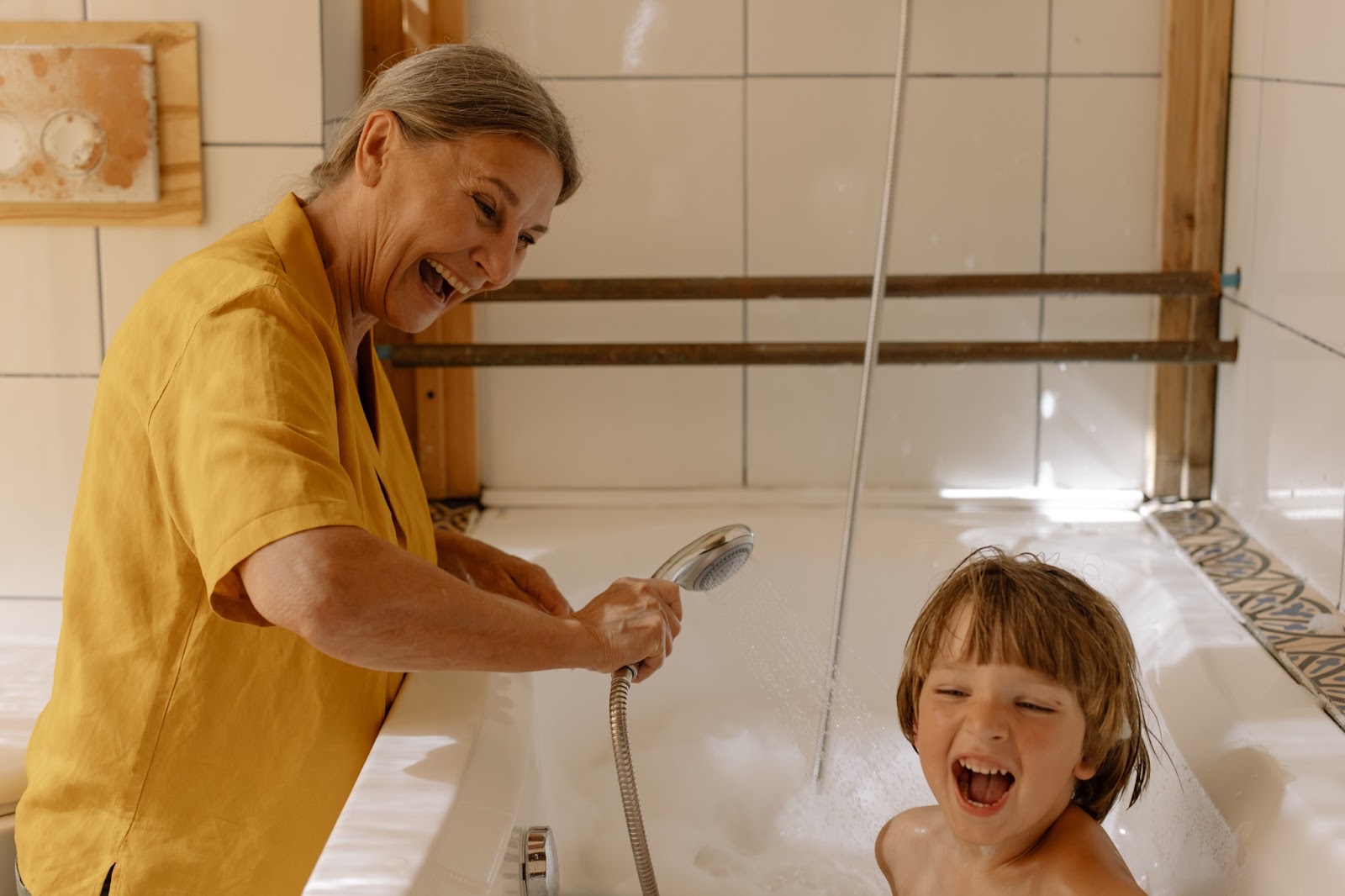 A grandmother sprays her grandchild with water in the bathtub. When traveling with small children, stick to routines like bath time.