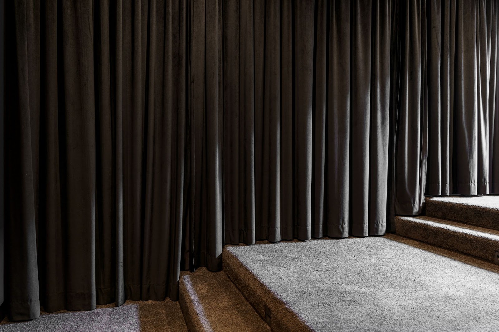 A home theater setup with plush carpeting and dark floor-to-ceiling curtains, creating a cozy, cinema-like environment with a raised platform for optimal viewing.