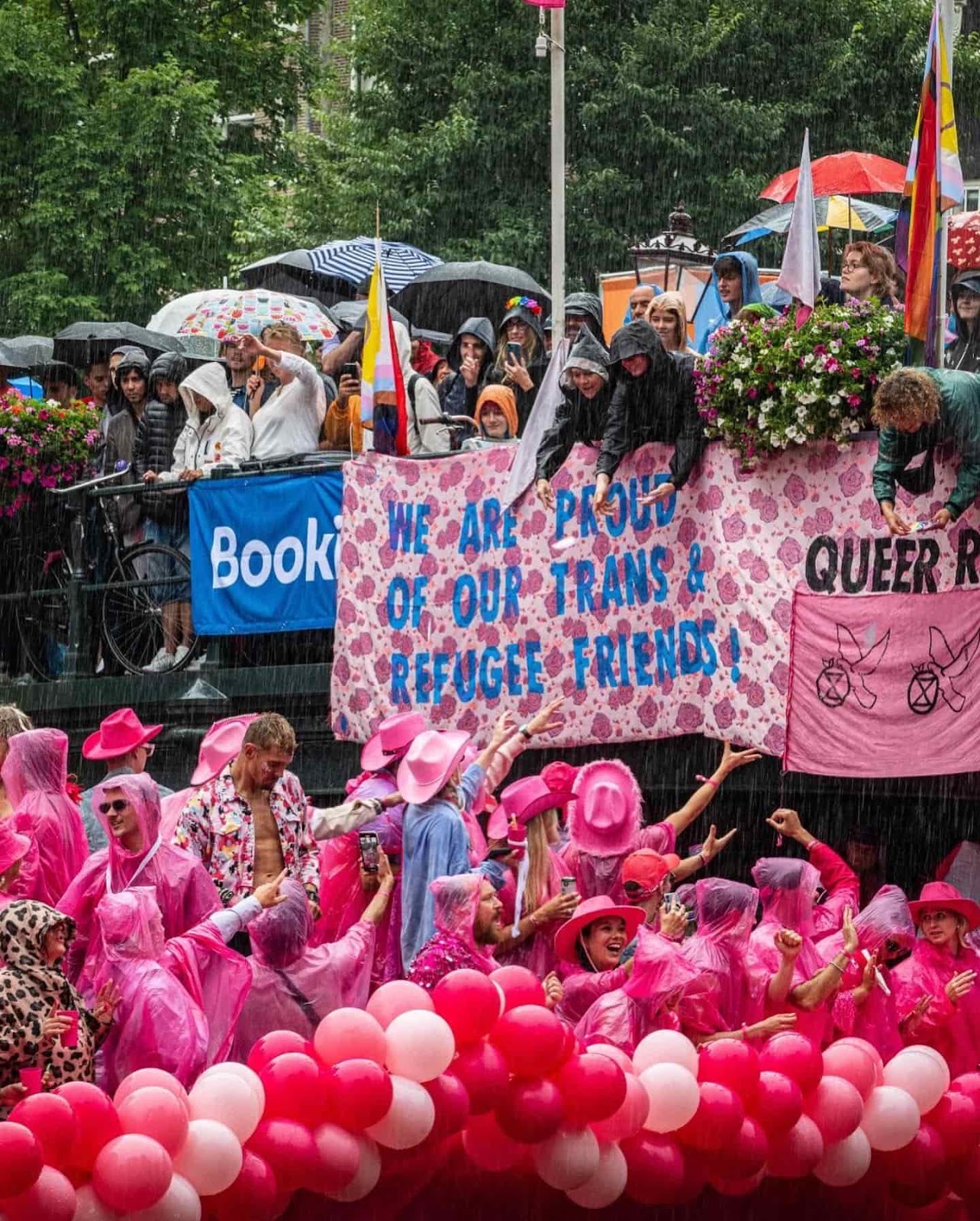 Rebels brave rain to drop a banner over a bridge as people in pink party below on a canal barge