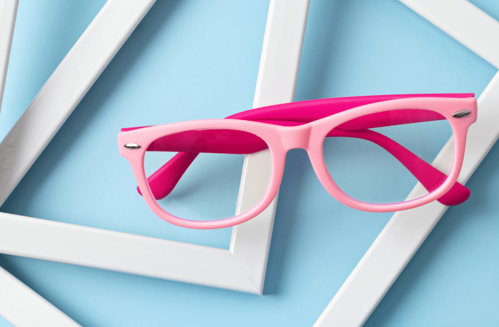 A pair of pink children's glasses sitting on a blue background with picture frames behind it