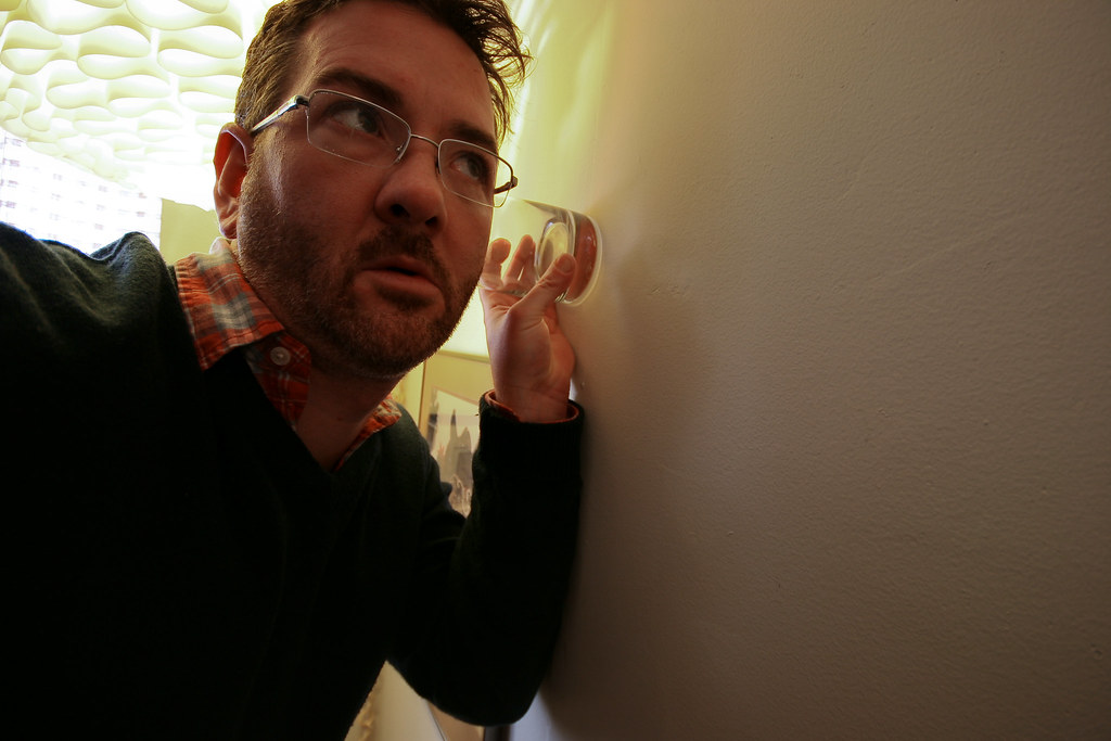 Hombre sosteniendo un vaso hasta una pared para tratar de escuchar a hurto