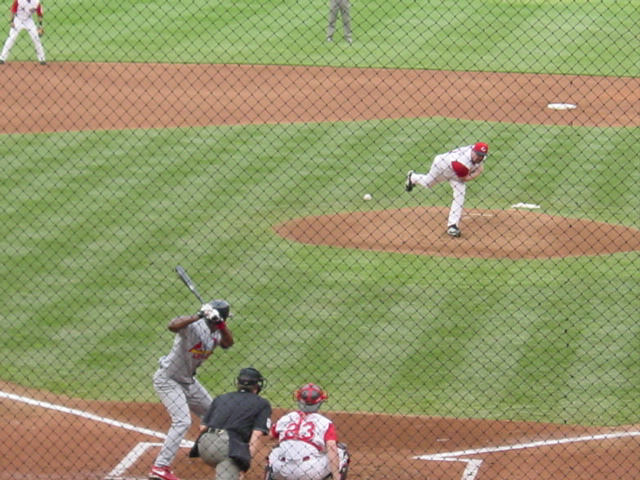 The pitcher has thrown the ball and it is in mid-air as the batter watches. 