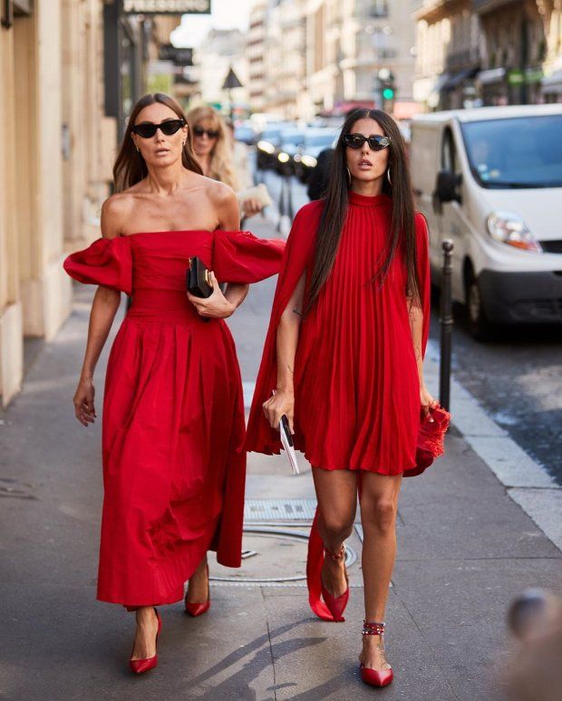 Duas mulheres brancas, em uma rua, com look monocromático vermelho. as duas estão de vestido e sapato de bico fino, usando óculos escuros. 